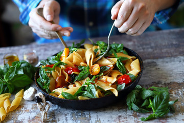 Selective focus. Chef's hands mix pasta with basil and tomatoes.