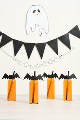 Decorated glasses with orange cocktail, garlands and paper ghost at Halloween party