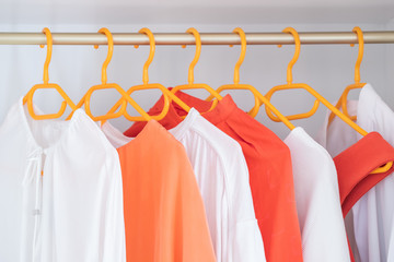 Coral and White colour clothes on hangers in wardrobe in dressing room. Several blouses and shirts for casual outfit. Fashion  background.