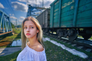 close-up portrait of a teen girl next to a passing train and a railway bridge