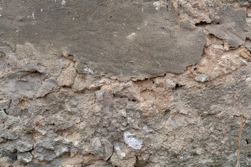 The texture of the old wall with a partially fallen off coating with the interior of a mixture of concrete with stones