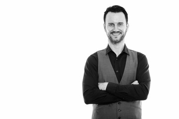 Studio shot of happy young man smiling and wearing vest with arms crossed