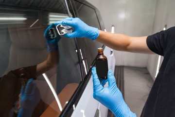 The process of applying a nano-ceramic coating for hydrophobic effect on the car's windows by a male worker with a sponge and - obrazy, fototapety, plakaty