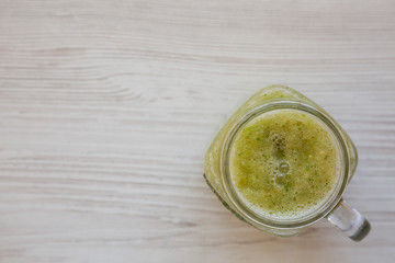 Homemade green cucumber apple smoothie in a glass jar on a white wooden table, top view. Flat lay, overhead, from above. Copy space.