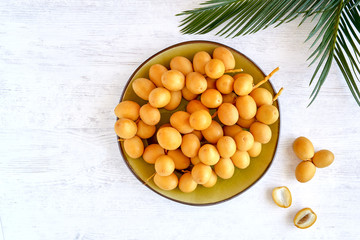 Fresh raw yellow dates in plate with palm leaf on white wooden background. Top view	