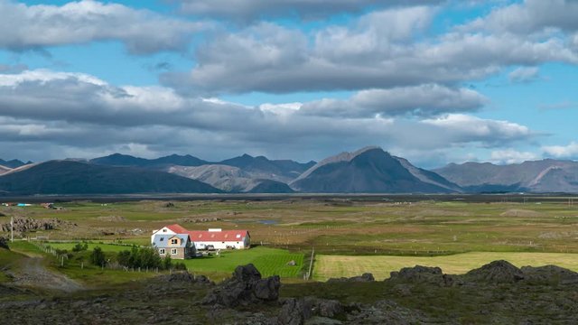 Clouds move over the mountains in Iceland. Farm on the plain. Time lapse. 4K