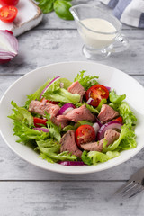 Salad with roast beef, tomato, onion, lettuce and mustard sauce on light background. Delicious healthy lunch with meat, diet food