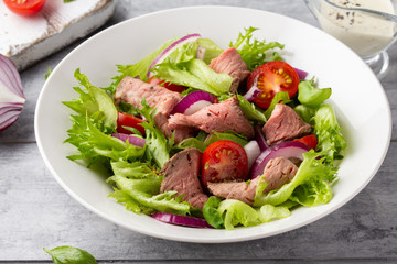 Salad with roast beef, tomato, onion, lettuce and mustard sauce on light background. Delicious healthy lunch with meat, diet food