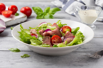 Salad with roast beef, tomato, onion, lettuce and mustard sauce on light background. Delicious healthy lunch with meat, diet food