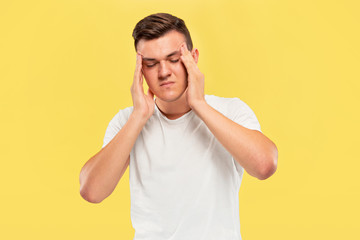 Caucasian young man's half-length portrait on yellow studio background. Beautiful male model in shirt. Concept of human emotions, facial expression, sales, ad. Suffering from headache, mental problems
