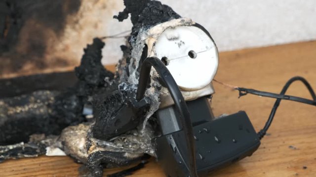 man takes out plug of electrical appliance from outlet of burned-out power strip.