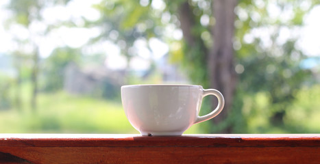 Close up white coffee cup on wood table and view of morning