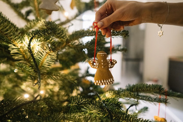 Female hand hangs angel gingerbread on the Christmas tree.