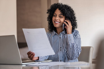 Smiling female entrepreneur talking on her cellphone and reading documents