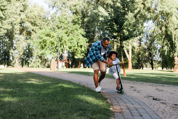 cheerful african american father near happy son on scooter