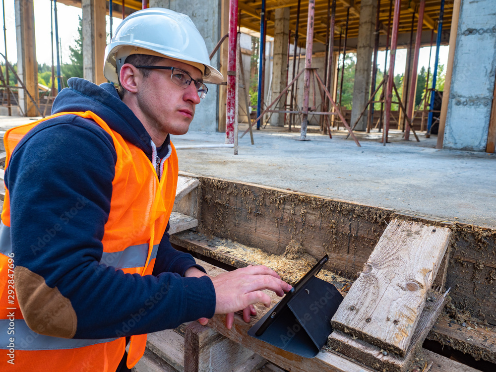 Poster a man with a tablet on the background of a building under construction. the builder controls the exe