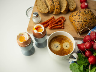 Pyszne, zdrowe śniadanie. Jajka na miękko z pieczywem, dodatkami i kawą leżące na białym tle....