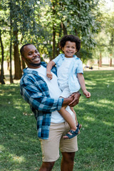 Fototapeta premium happy african american man holding in arms cute curly kid