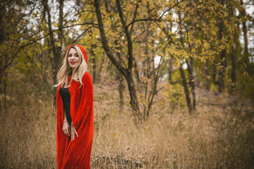 Concept of Halloween. Beautiful and simple costume of little red hood. Mysterious hooded figure in misty forest. Girl in red raincoat. Cosplay Fairy Tale Little Red Riding Hood 