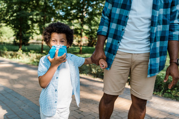 Fototapeta premium cropped view of african american man holding hands with cute son covering face with present