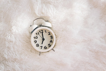 Retro alarm clock showing seven o'clock at the morning lying on the bed