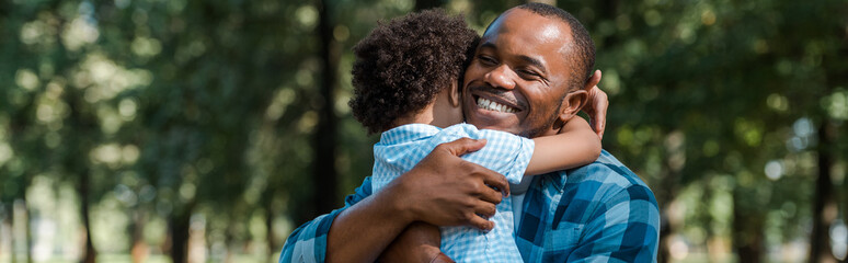 panoramic shot of happy african american father hugging son - Powered by Adobe