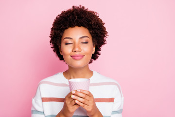 Photo of pretty dark skin lady holding in hands hot beverage cup dreamy closing eyes enjoy good...