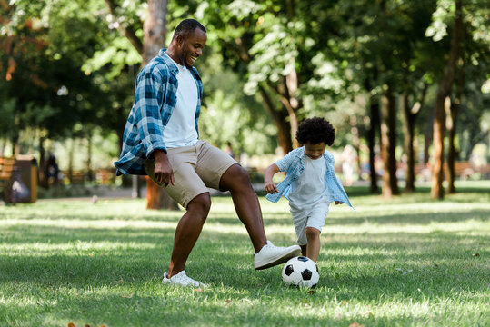 Happy African American man playing football with curly son