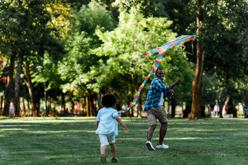 selective focus of happy african american father looking at son while running with kite