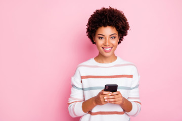 Photo of pretty dark skin curly lady holding telephone addicted to internet reposts and comments wear white striped pullover isolated pastel pink color background