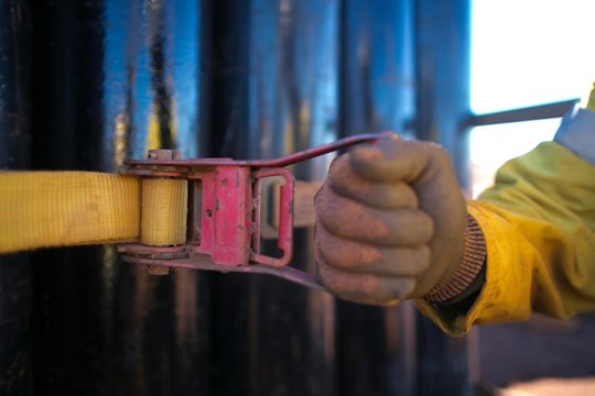 Male hand wearing a safety glove using ratchet faster, securing the load 