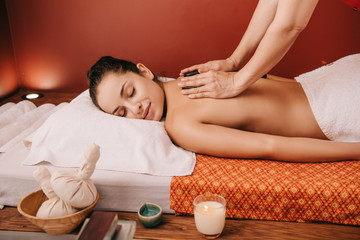 Fototapeta na wymiar cropped view of masseur doing hot stone massage to woman in spa salon