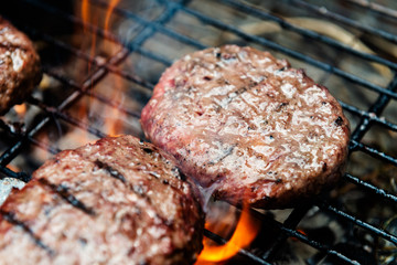 Burgers are cooking on grill with open flames