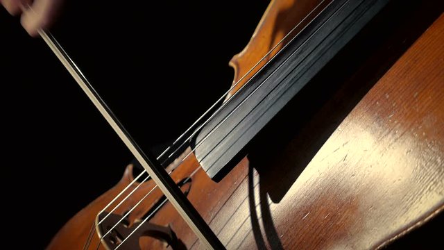 Woman in black plays on cello, black background