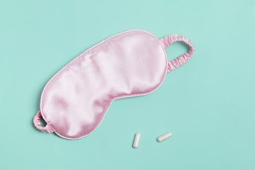 Sleeping mask and pills on pastel green background.