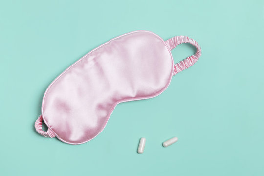 Sleeping mask and pills on pastel green background.