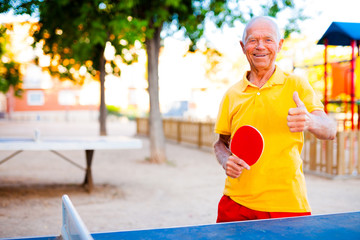 Happy mature man playing table tennis and showing thumb up