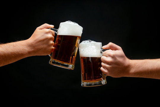 Hands toasting with beer on black background