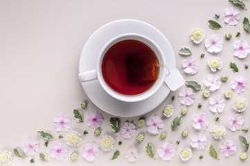 Obraz na płótnie Canvas White ceramic cup with tea on a corner floral pattern on a beige background. Flower tea concept. Tea bag. Top view