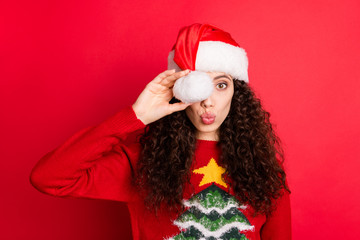 Close-up portrait of her she nice attractive lovely cute girlish funny cheerful wavy-haired Santa girl pout lips hiding eye behind hat ball isolated on bright vivid shine vibrant red color background