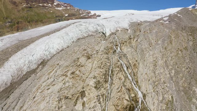 Aerial shot climbing over mountain stream and towards crevassed glacier