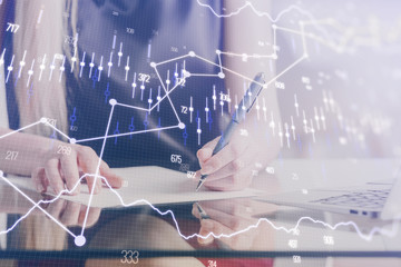 A woman hands writing information about stock market in notepad. Forex chart holograms in front....