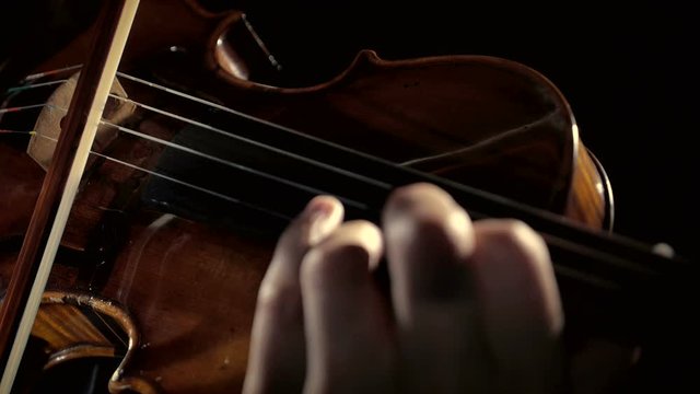 A man plays the violin in a dark room. Black background.