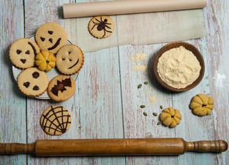 Homemade cakes for Halloween. Cornmeal, rolling pin, pumpkin seeds, baking paper, cookies with spiders, bats, pumpkins, scary smiles, cobwebs on a light blue wooden background.