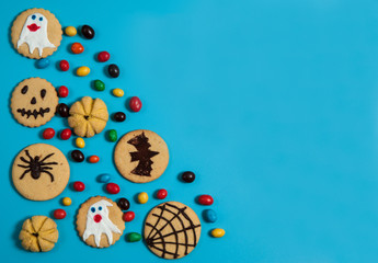 Composition for Halloween. The pattern is made of colorful candies, homemade cookies with pumpkins, bats, cobwebs, spiders, ghosts on a blue background.