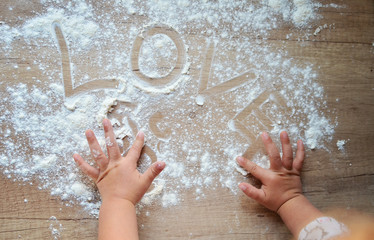 Little hands of girl making dough and writing love on the wooden board with flour. Christmas...