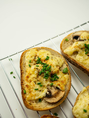 Kromki zapiekane z serem, pieczarkami i szczypiorkiem. Zbliżenie.