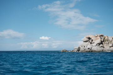 Seascape view from boat with anthropomorphic rock formation in a sunny day and clear blue sky and clouds in Sardinia.