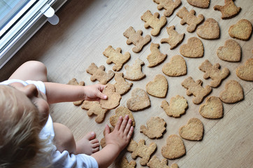 Little hand with handmade cookie in brown color. Christmas gingerbreads on the wooden table. Different shapes. Top view.
