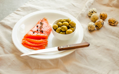 Slices of Salted Raw fish fillet with olive, quail eggs on white plate. Keto diet concept. Ketogenic diet food frame. Balanced low-carb food. Selective focus
